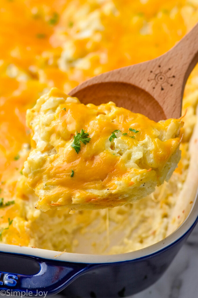 Close up view of wood spoon serving hashbrown casserole from baking dish