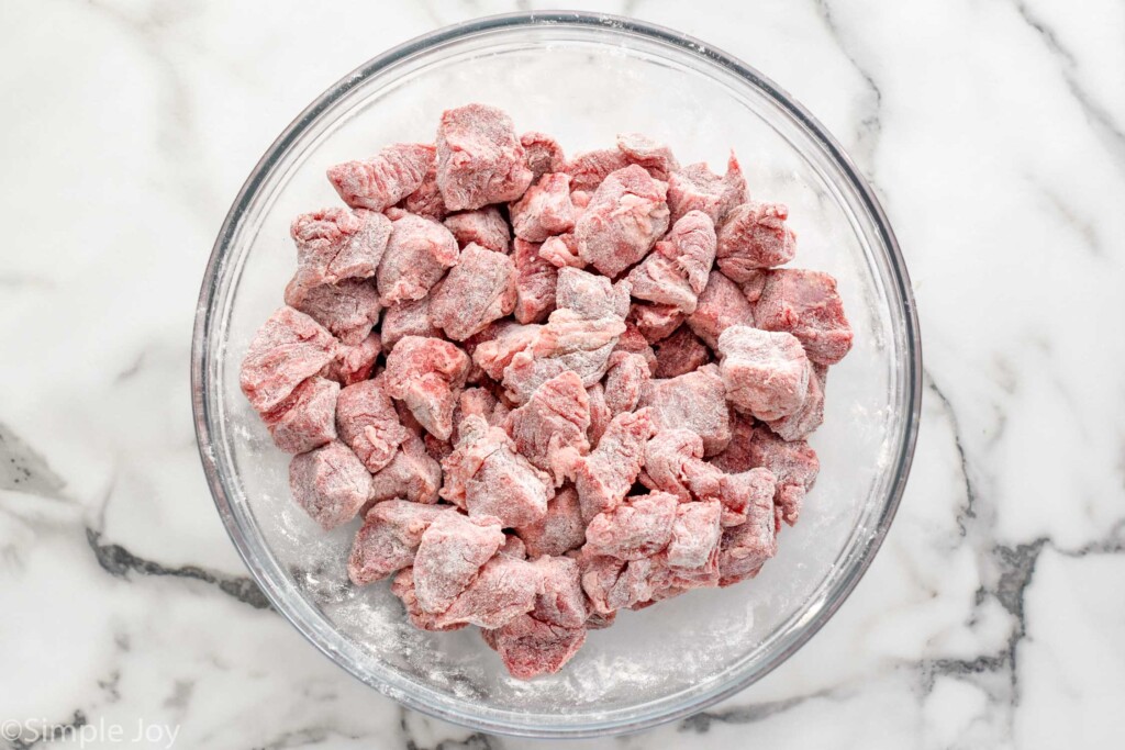 Overhead view of a glass mixing bowl of beef being prepared for Crockpot Beef Stew recipe.