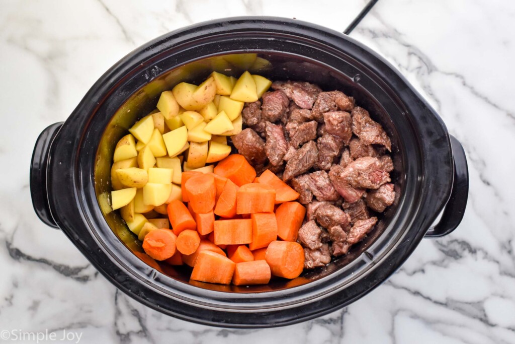 overhead of a slow cooker with the ingredients for beef stew before cooking