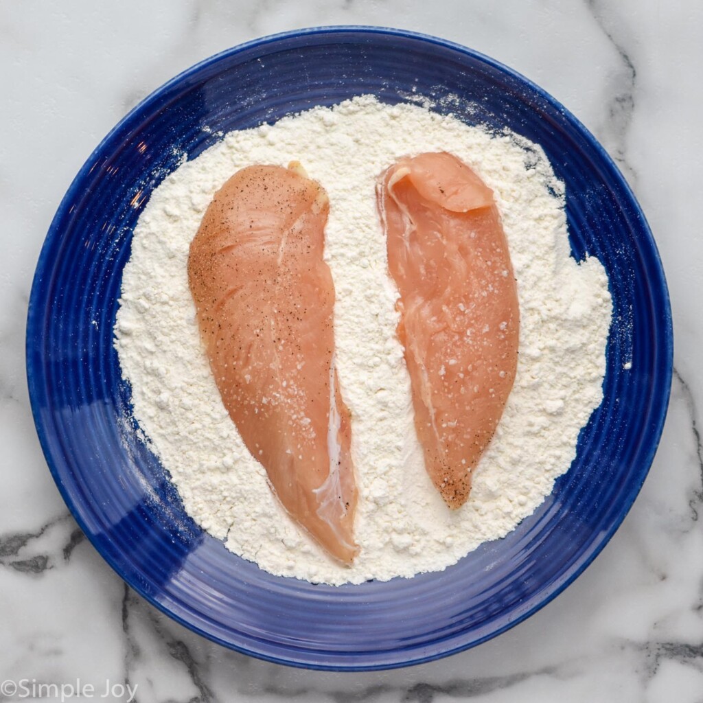 overhead of plate of flour mixture and chicken tenders to make Baked Chicken Tenders