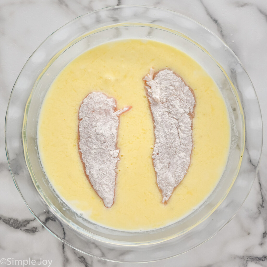 overhead of glass bowl of egg mixture with two chicken tenders to make Baked Chicken Tenders