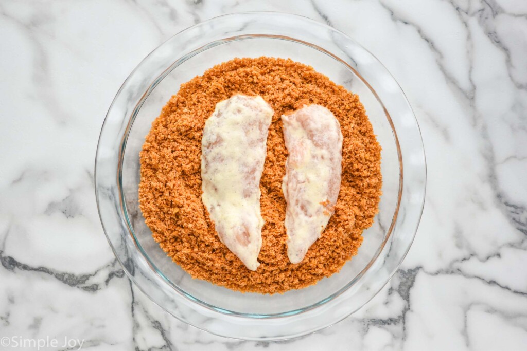 overhead of glass bowl of breading and raw chicken to make Baked Chicken Tenders