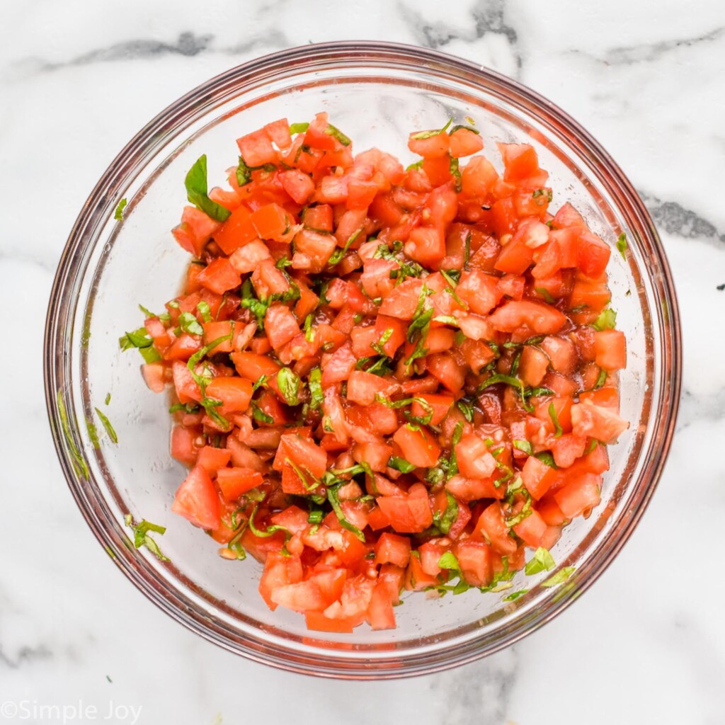 Overhead view of a mixing bowl of diced tomatoes and ingredients for Bruschetta recipe.