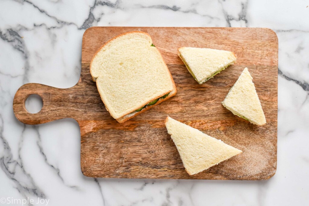 overhead of wooden cutting board with a whole cucumber sandwich and cut cucumber sandwich