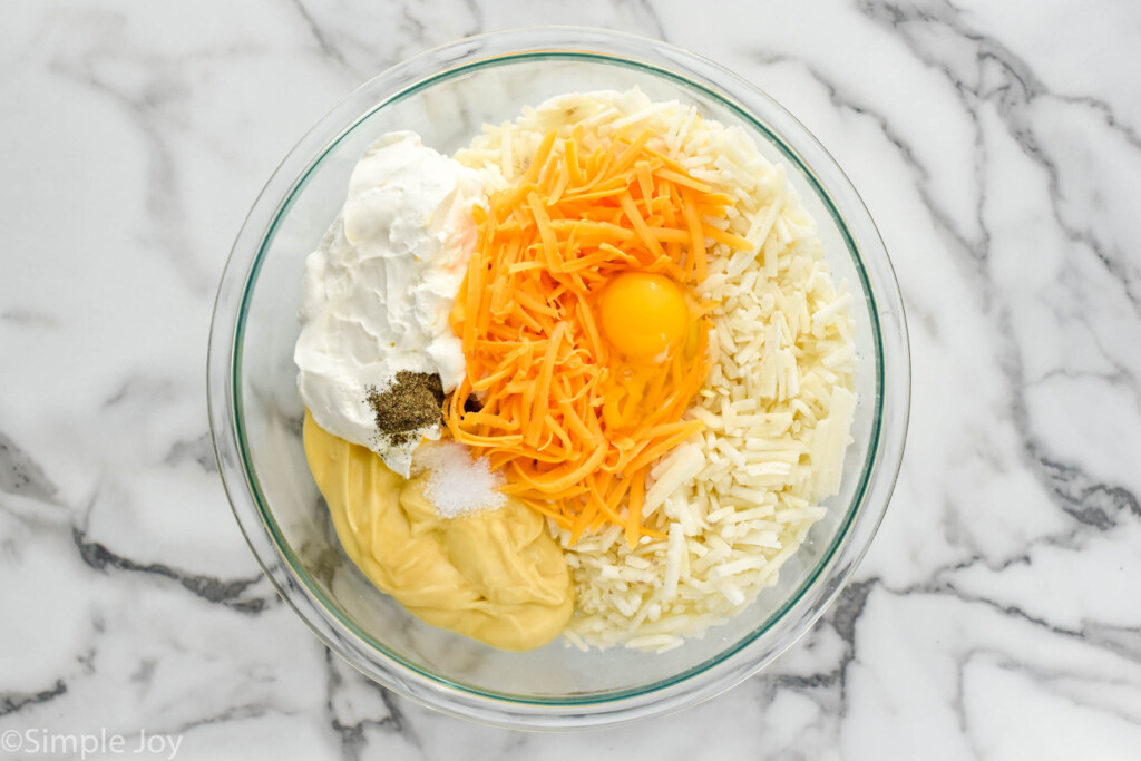 Overhead view of a glass mixing bowl of ingredients for hashbrown casserole recipe.