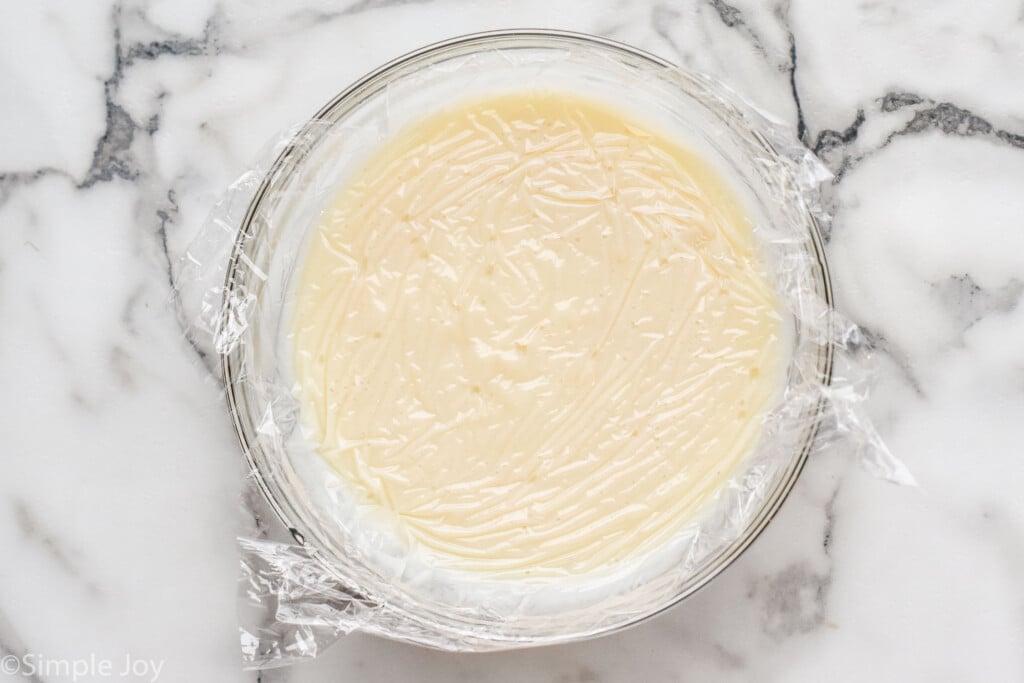 Overhead view of a mixing bowl of Pudding recipe with plastic wrap covering the bowl.