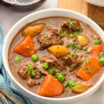 Bowl of Crockpot Beef Stew with silverware and a glass of red wine beside