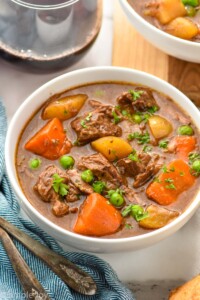 Bowl of Crockpot Beef Stew with silverware and a glass of red wine beside