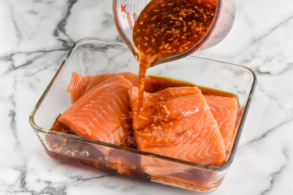 Photo of measuring cup of marinate being poured over glass container of salmon for Teriyaki Salmon recipe.