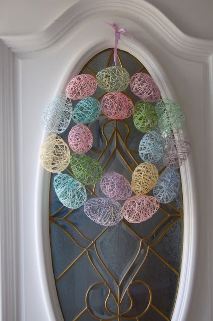An Easter Egg Wreath made with embroidery floss eggs hanging on a white door.