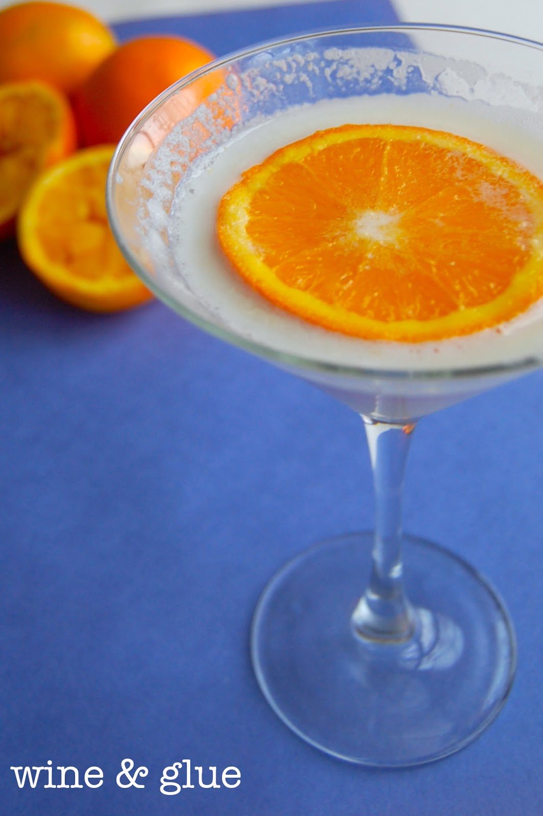 A glass of Orange Dreamsicle Martini that is an opaque white color with a circular slice of an orange. 